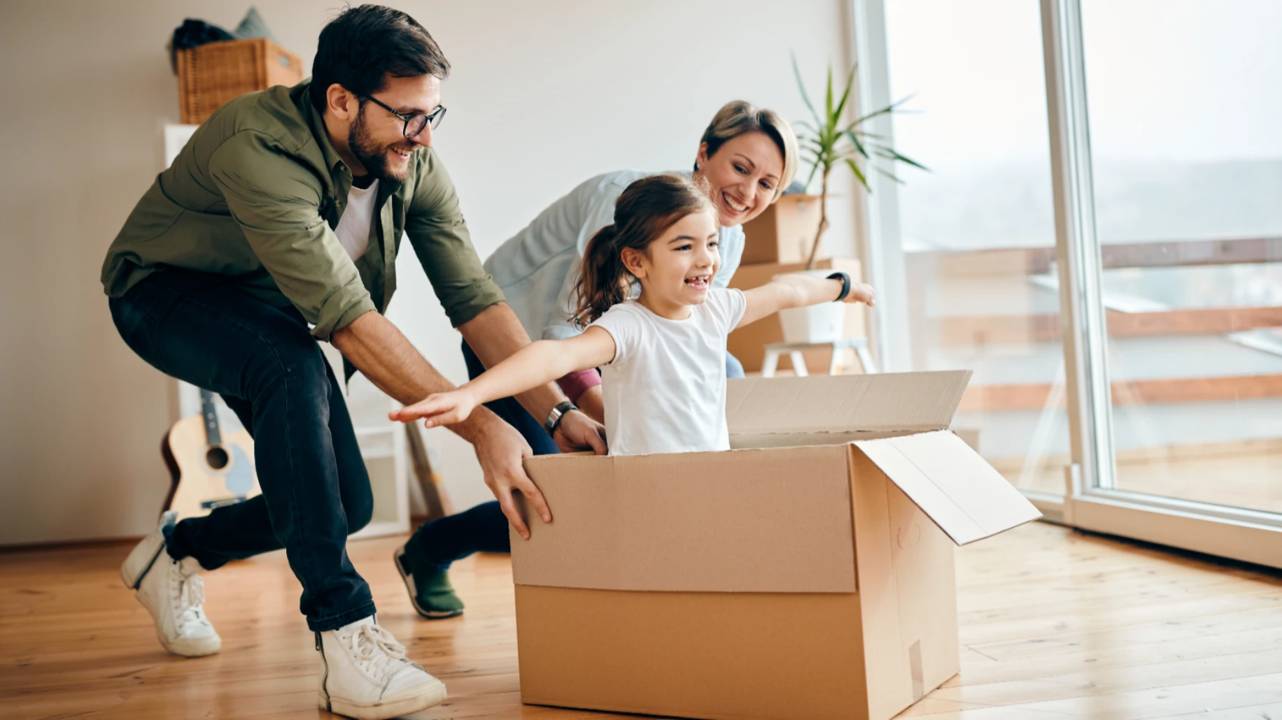 Happy family playing with a cardboard box while packing in their Paris apartment